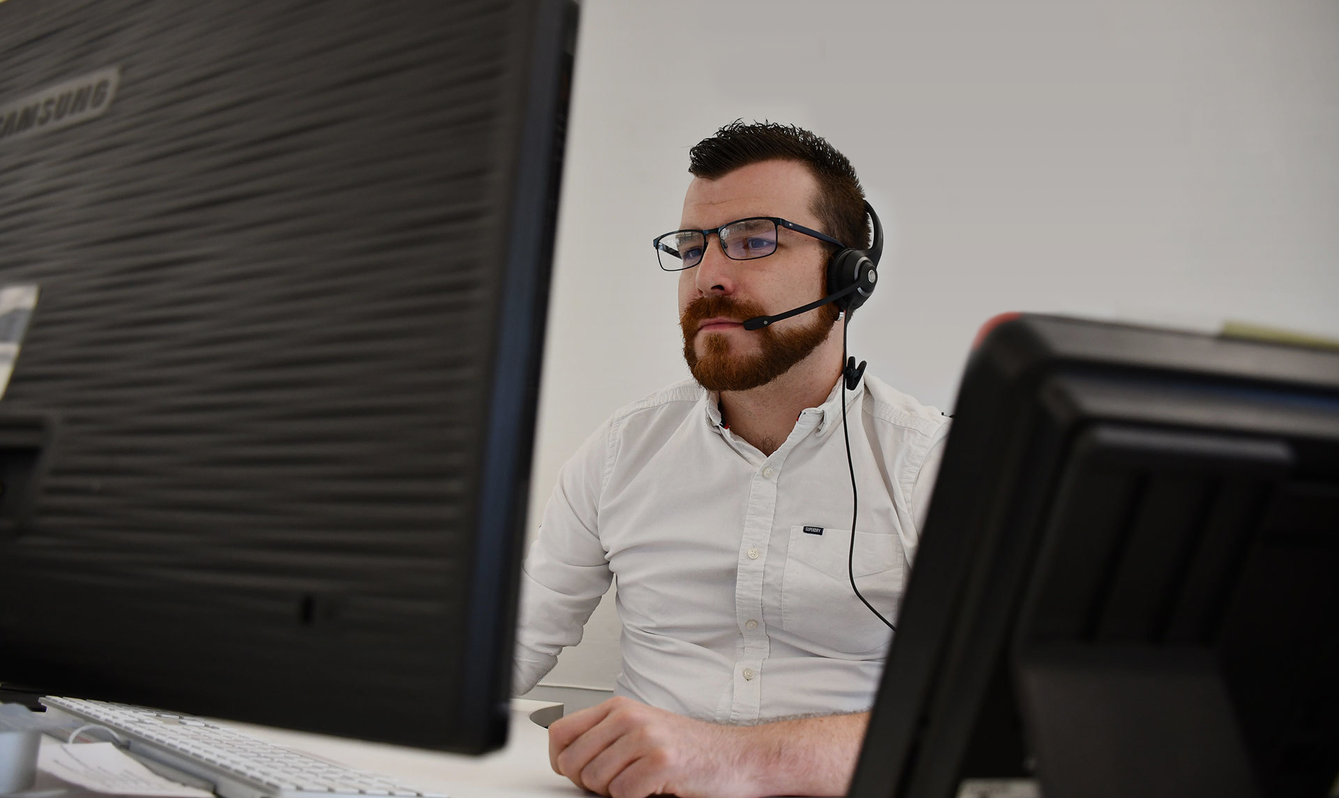 A man wearing a headset, looking at his computer screen